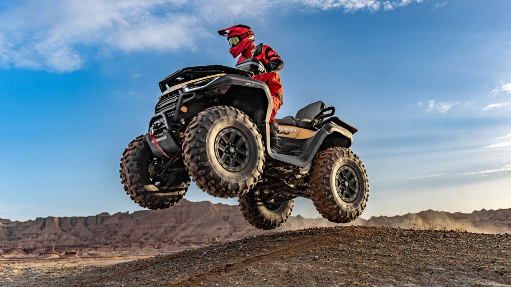 En förare kör Segway Snarler AT10 i ett hopp över ett stenigt landskap. Fyrhjulingens robusta fjädring och prestanda i luften visas tydligt i bilden.