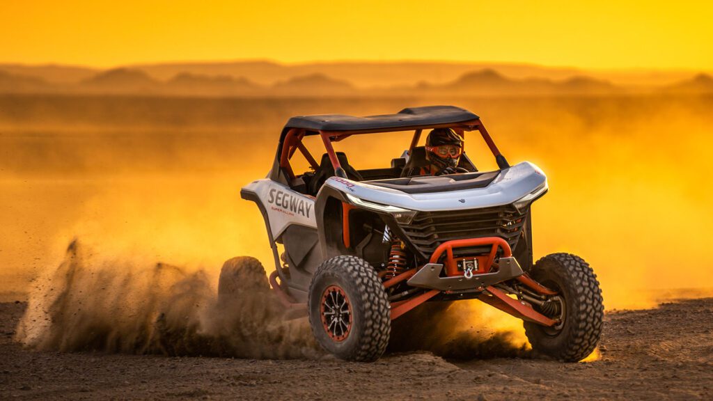 Segway Villain SX10 körs genom sanddyner i hög fart med tydliga spår i terrängen. Bilden visar fordonets kontroll och sportiga design i ökenmiljö.