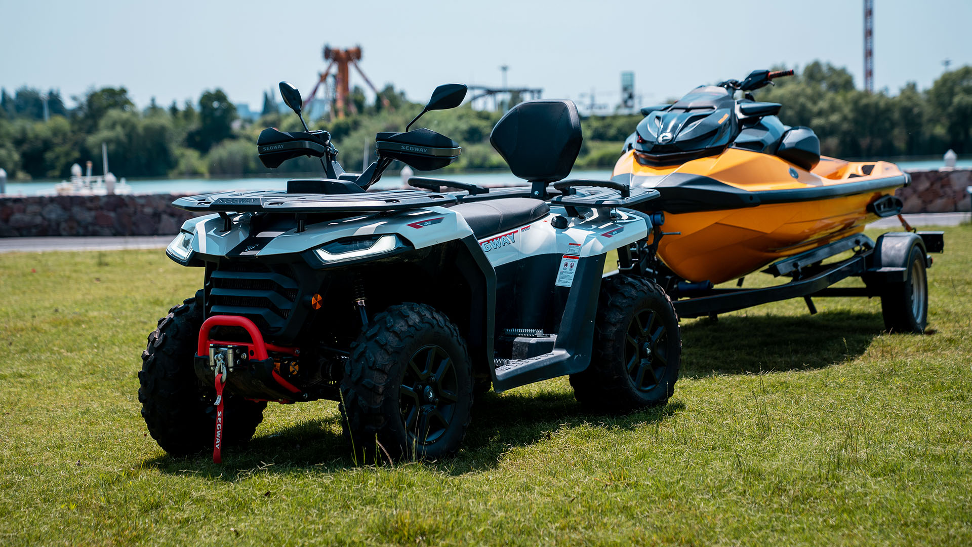 Segway Snarler AT5 står på gräsmatta och drar en vattenskoter på trailer, redo för äventyr.